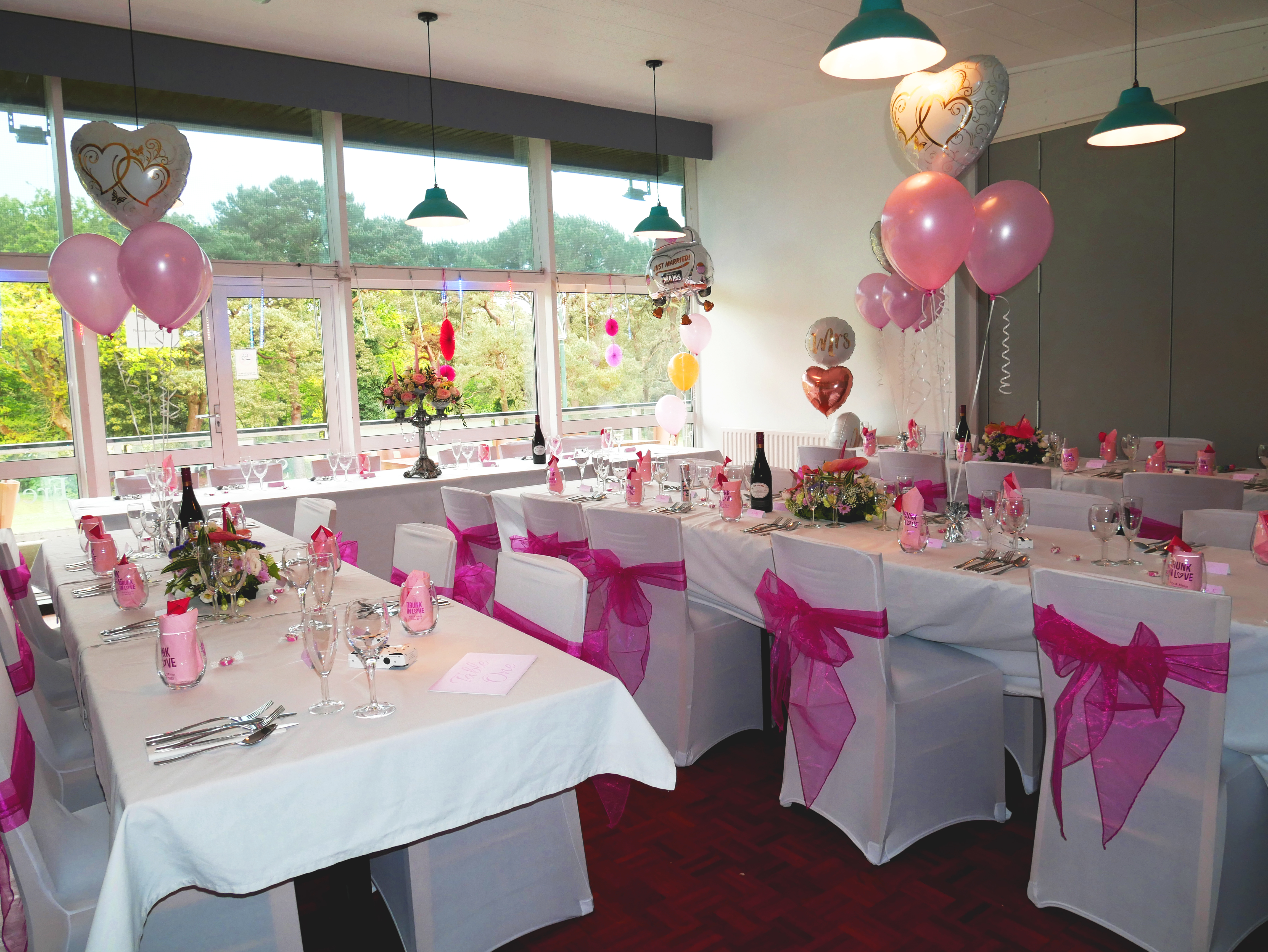 Tables and chairs dressed up for an event in white with pink bows and balloons