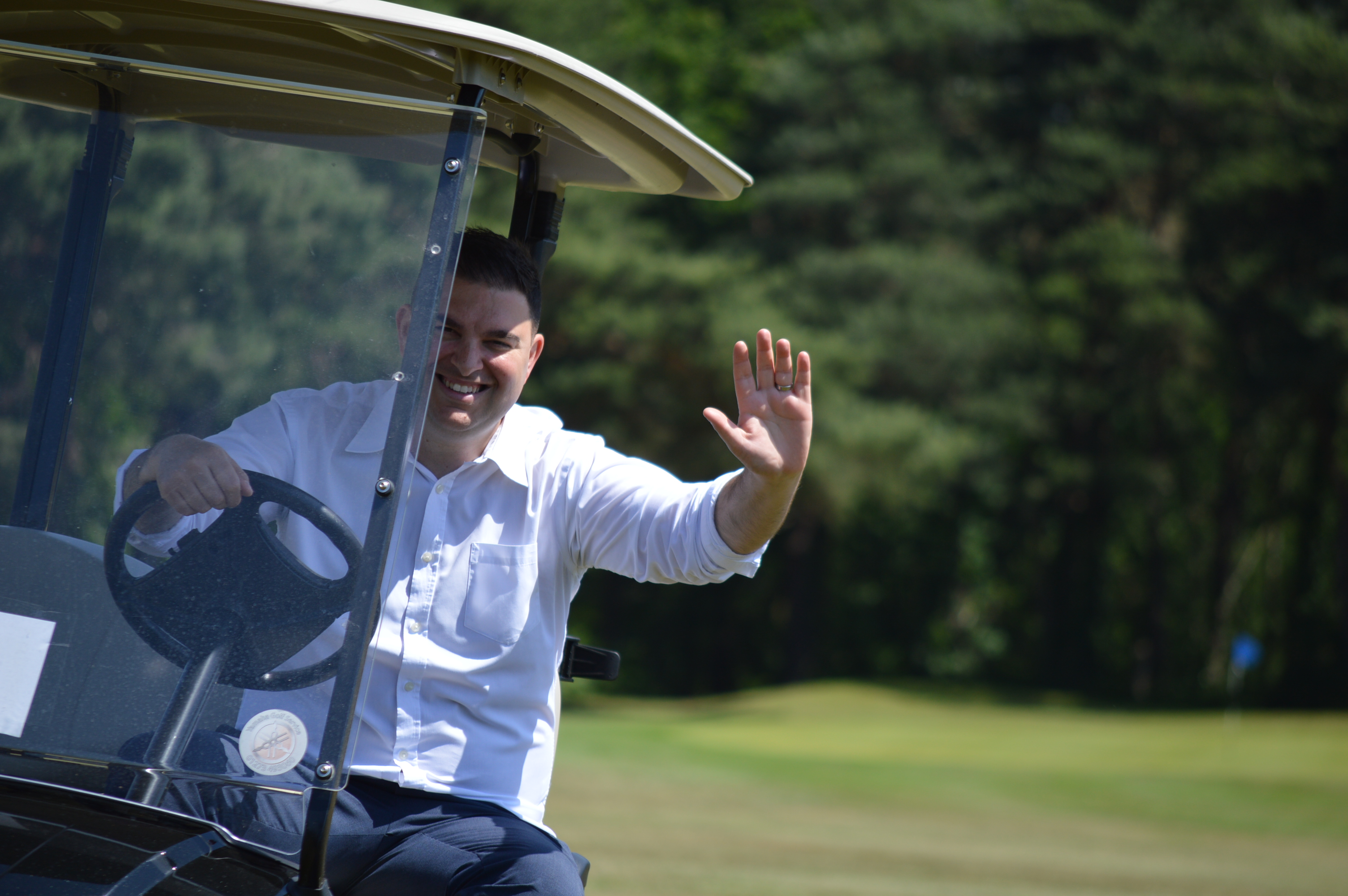 A person waving from a golf buggy