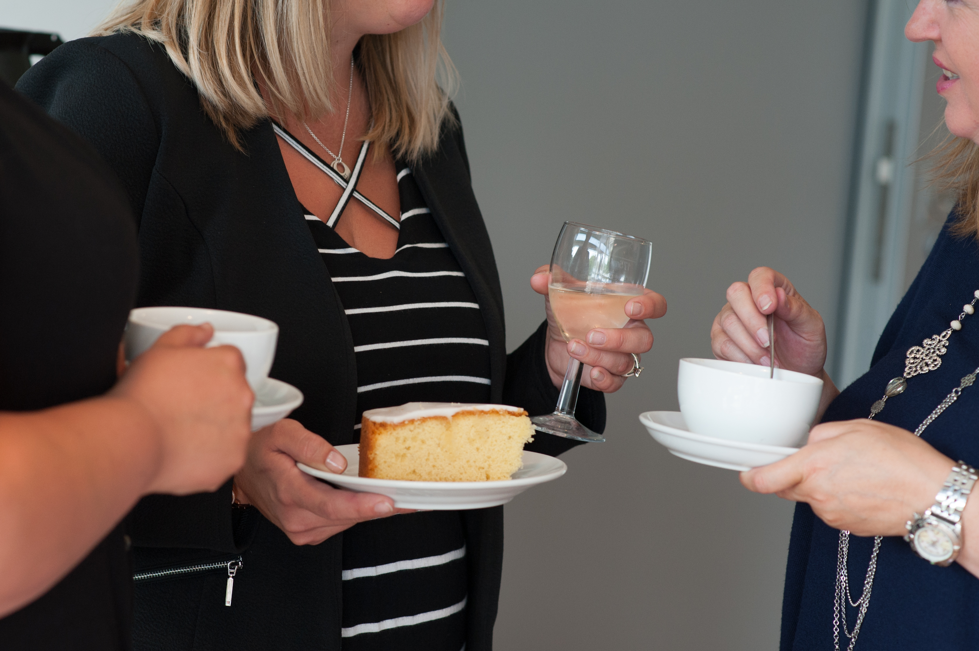 People standing and talking, holding drinks and cake
