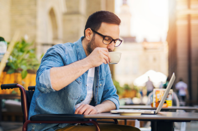 Man drinking coffee using laptop in a wheelchair