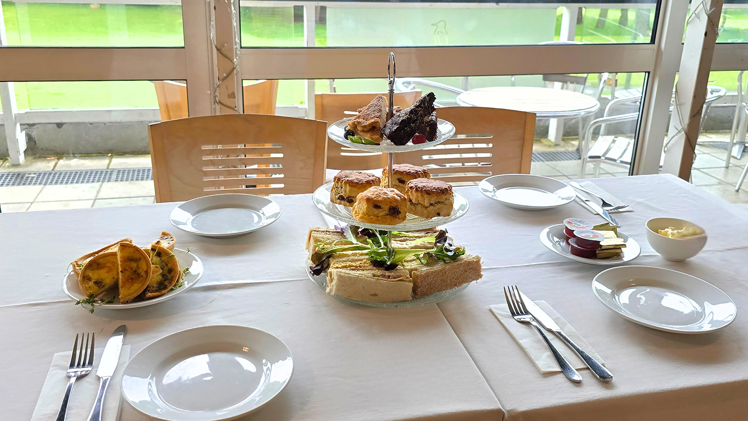 Table dressed for afternoon tea with cake stand, sandwiches, scones, jam and cream.