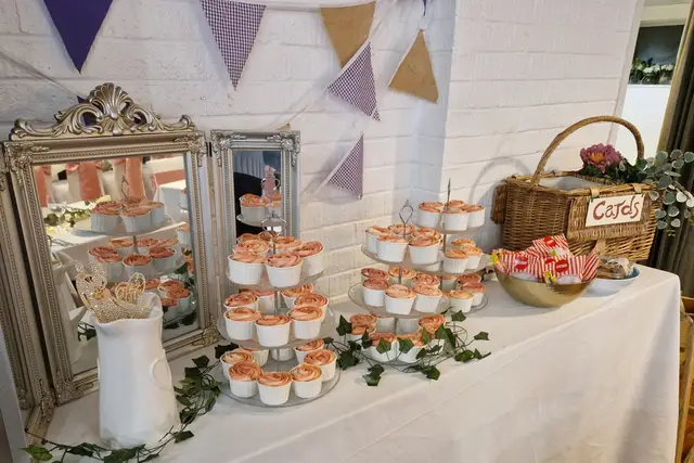Wedding cupcakes displayed on table with flowers and hanging bunting.