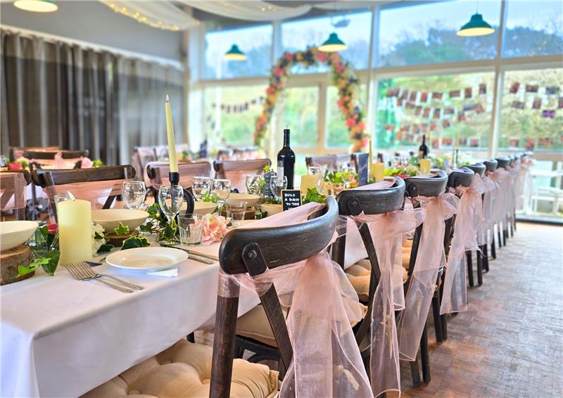 Dining tables and chairs dressed with ribbon and flowers for wedding reception.